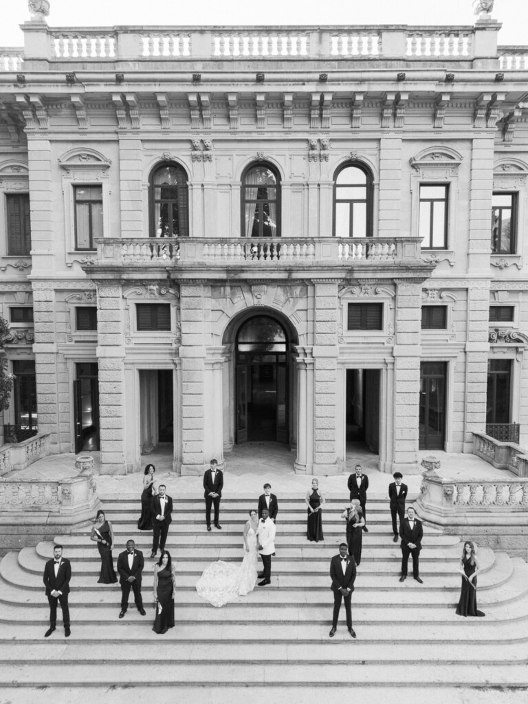 Black and white portrait of Fran, Ope and their wedding party on the steps of Villa Erba, Lake Como.