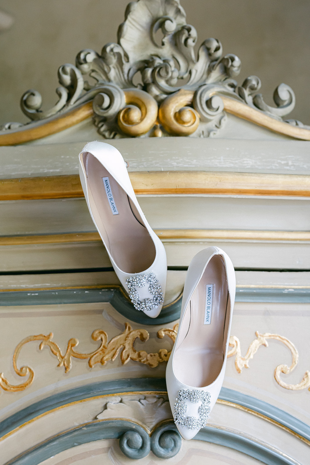 Embellished bridal pumps displayed on an ornate painted cabinet at Villa Erba.