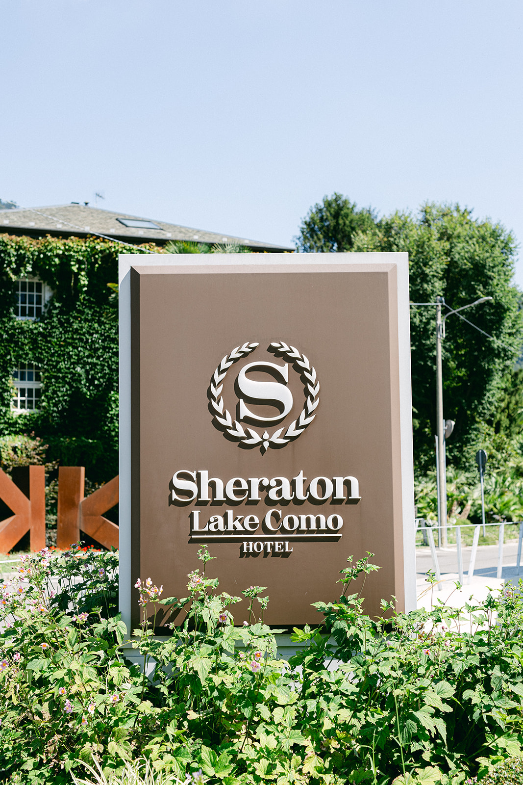 Sheraton Lake Como Hotel sign surrounded by greenery before Fran and Ope's wedding.