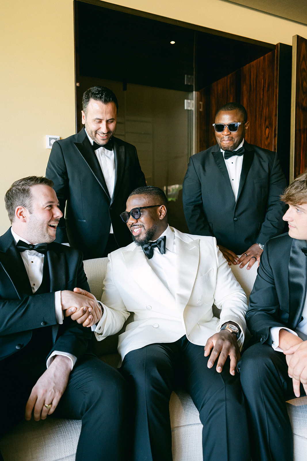 Ope laughing with his groomsmen while wearing his ivory wedding jacket.