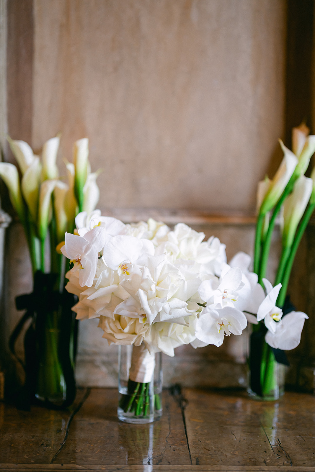 White bridal bouquet with calla lilies and orchids resting on a wooden table.