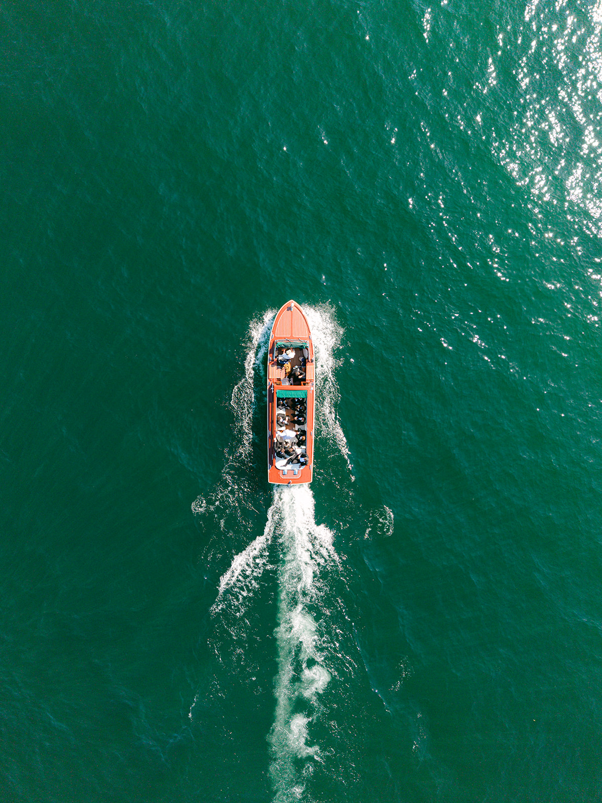 Aerial view of a wooden motorboat cruising through the turquoise waters of Lake Como.