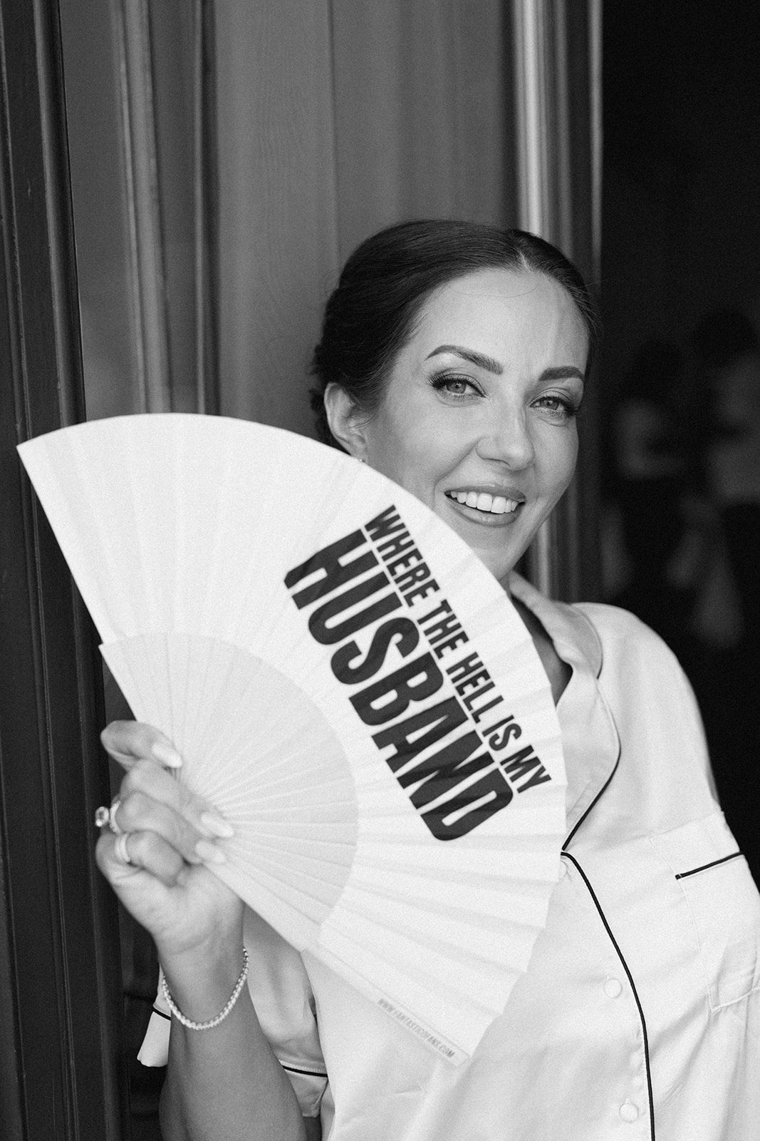 Black and white portrait of Fran smiling behind a wedding fan during her bridal preparations.