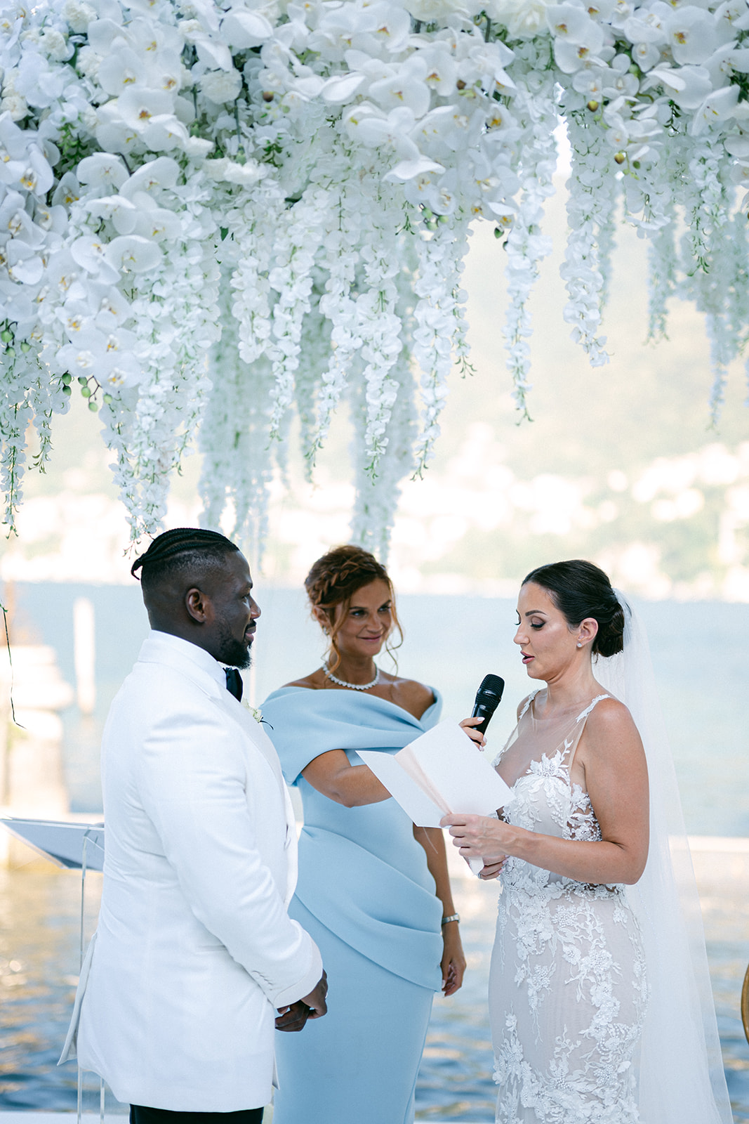 Fran and Ope exchanging vows with their officiant beneath cascading white flowers.
