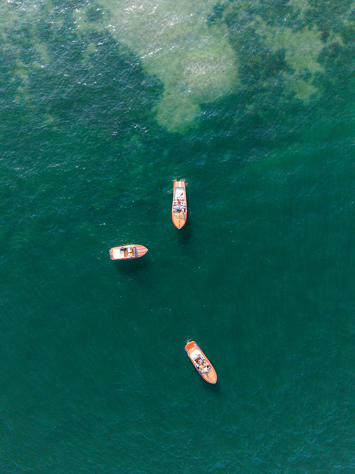 Aerial view of three wooden boats on the emerald waters of Lake Como.