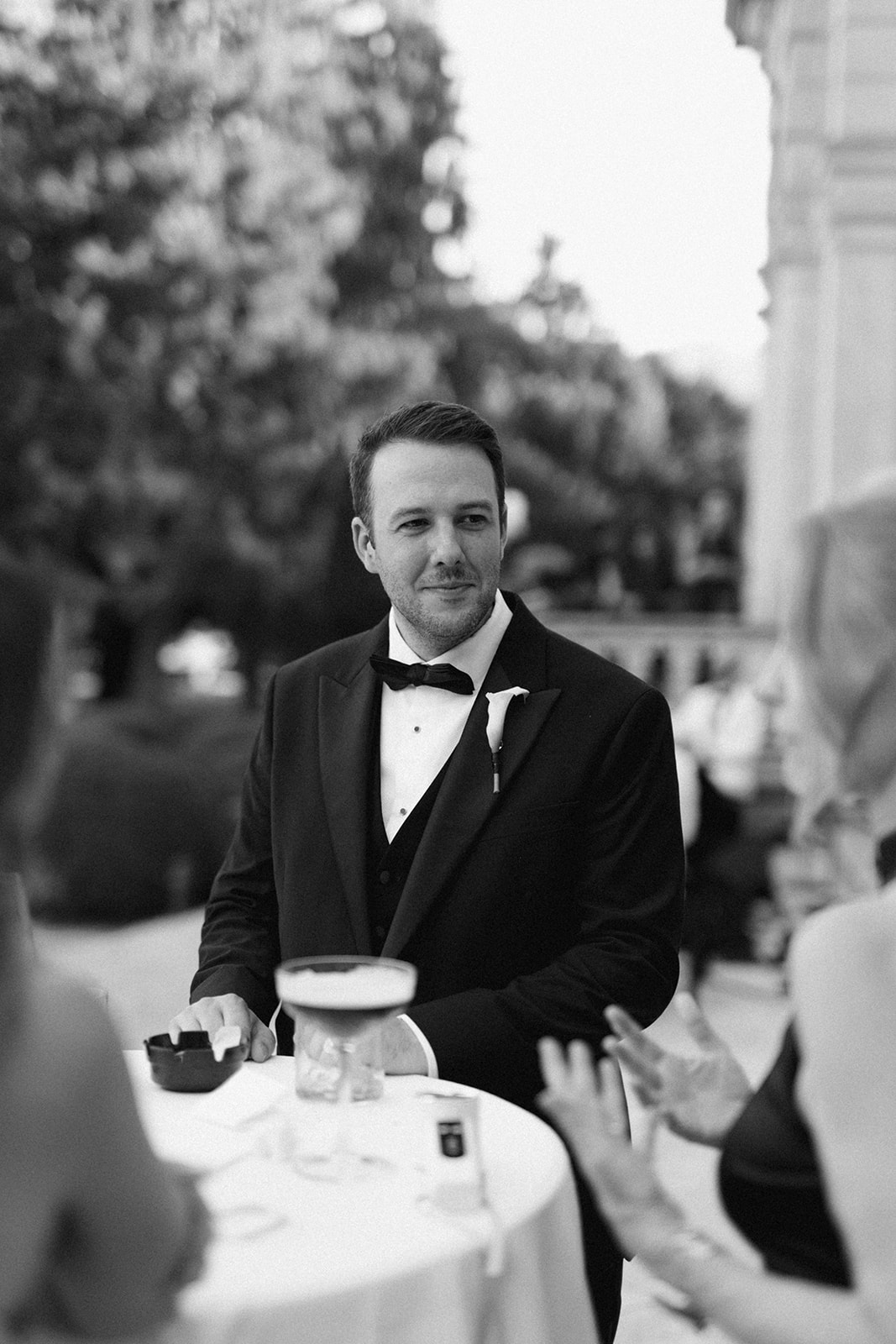 Black and white portrait of a wedding guest in a tuxedo holding a glass at Villa Erba.