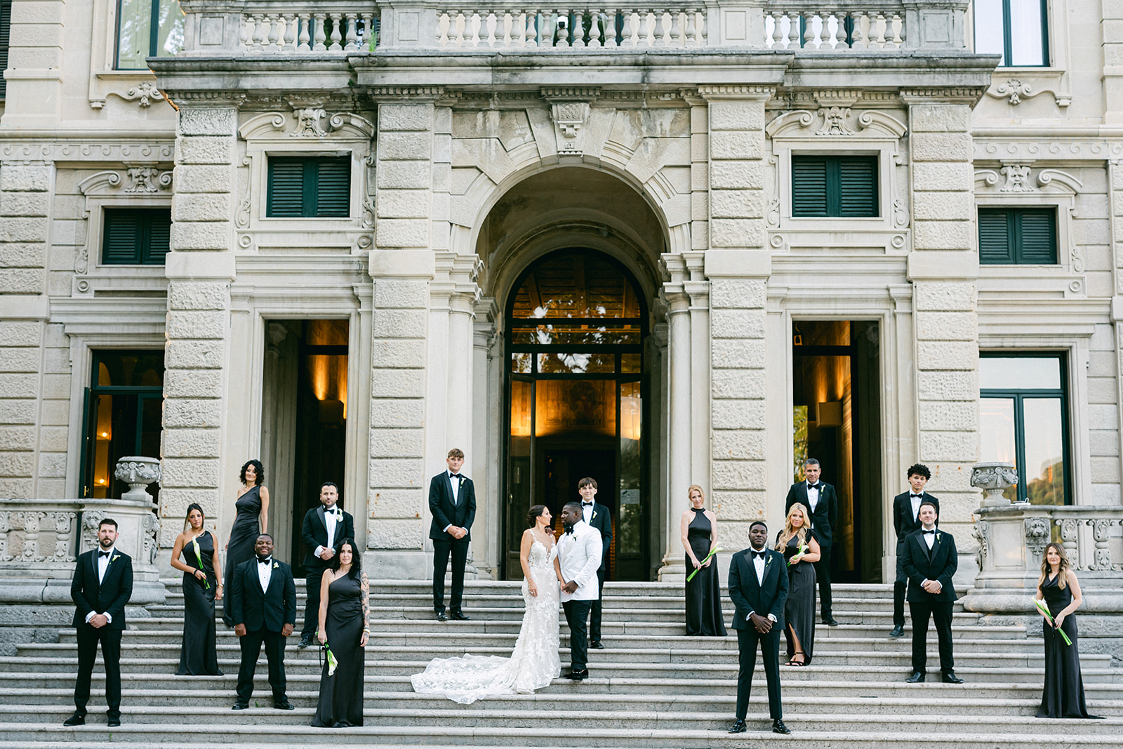 Fran and Ope with their wedding party arranged across the grand entrance steps of Villa Erba.
