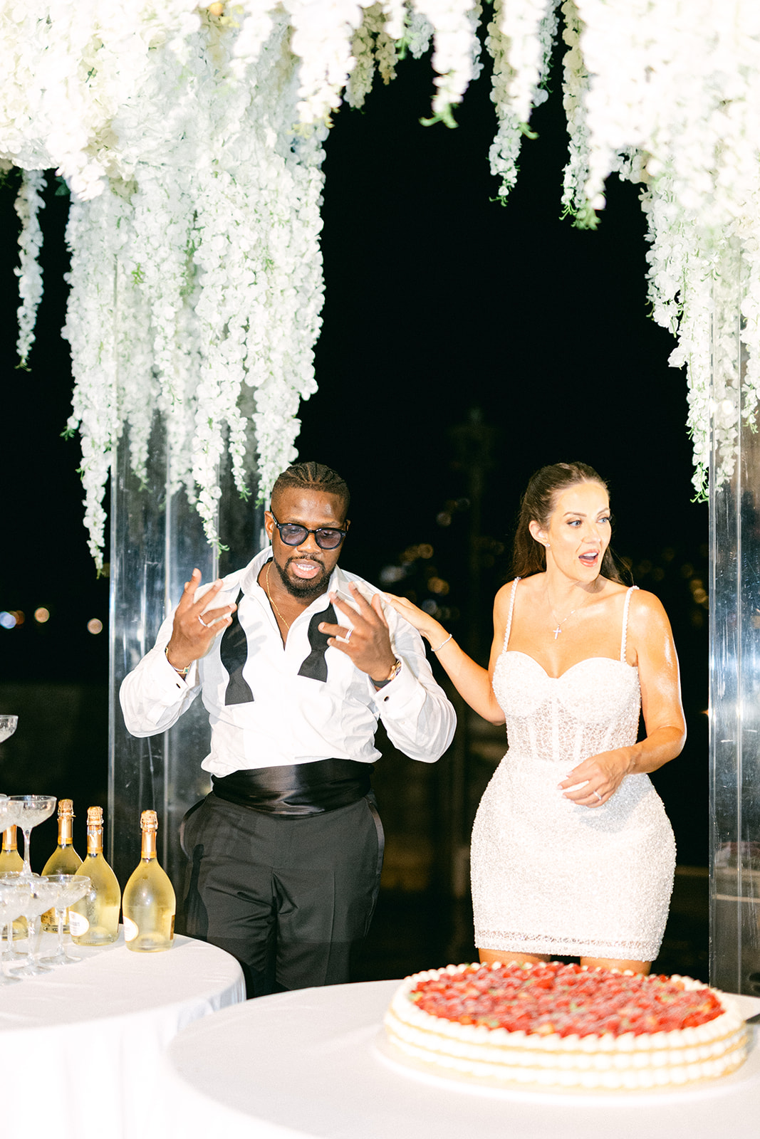 Fran and Ope raising champagne glasses beside their strawberry wedding cake.