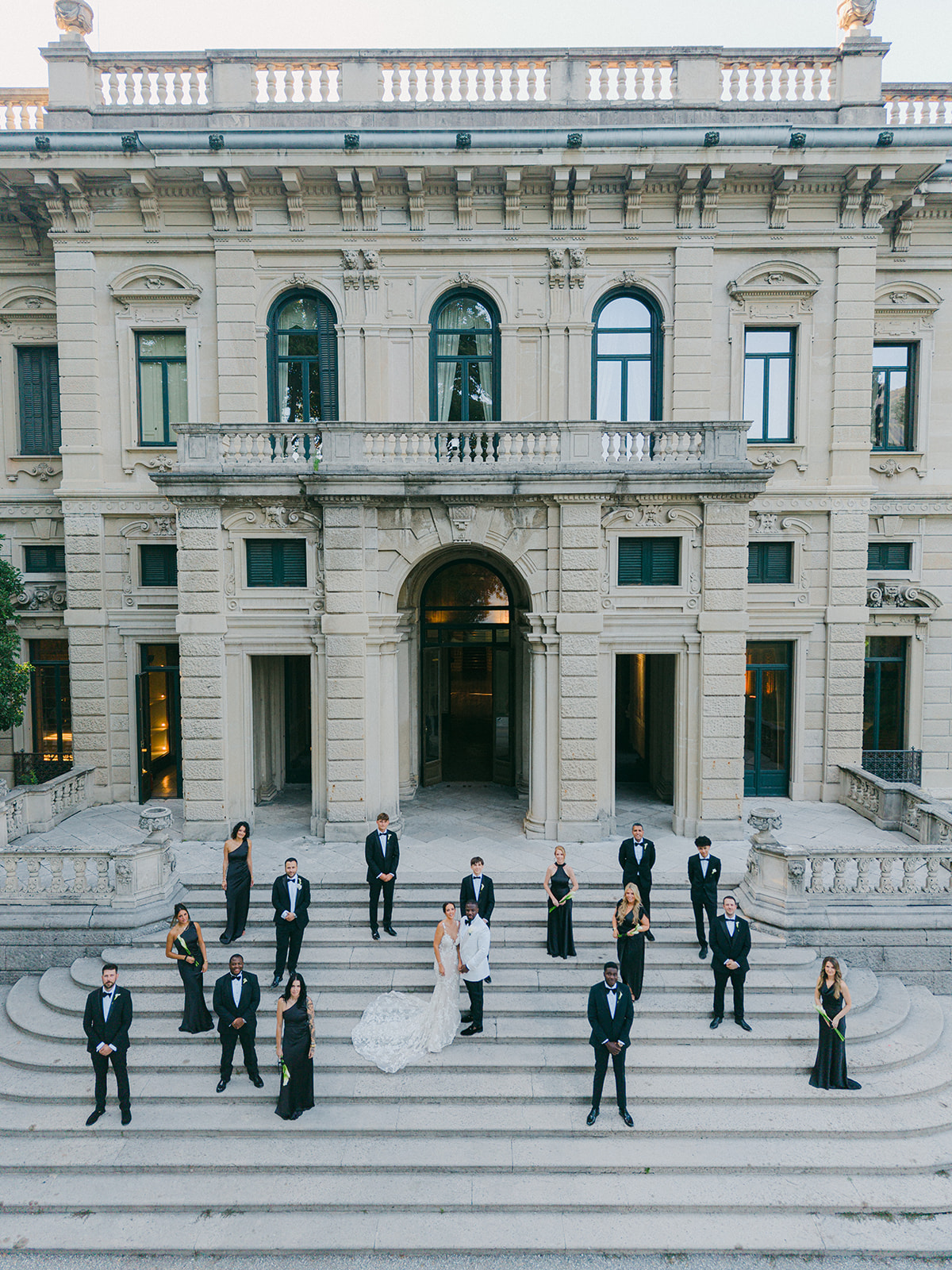Fran and Ope with their wedding party on the steps beneath Villa Erba's ornate facade.