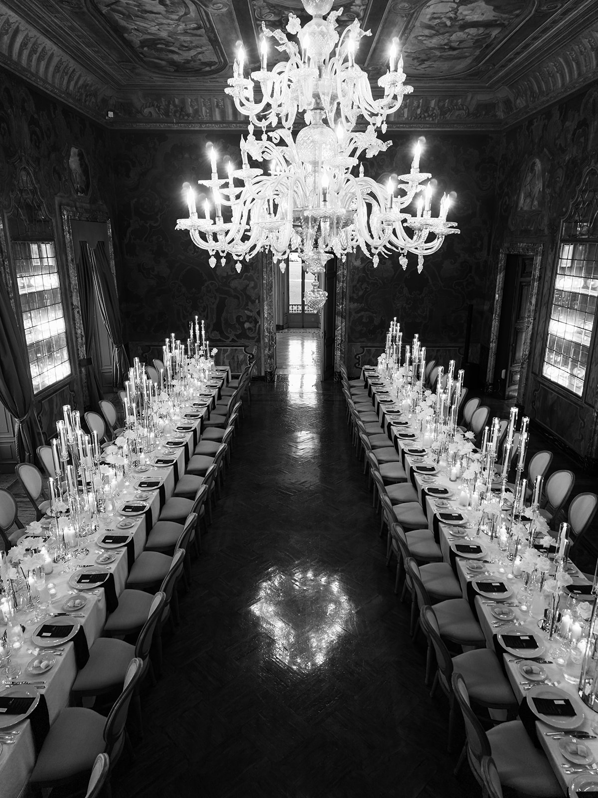 Black and white view of long wedding reception tables beneath chandeliers at Villa Erba.