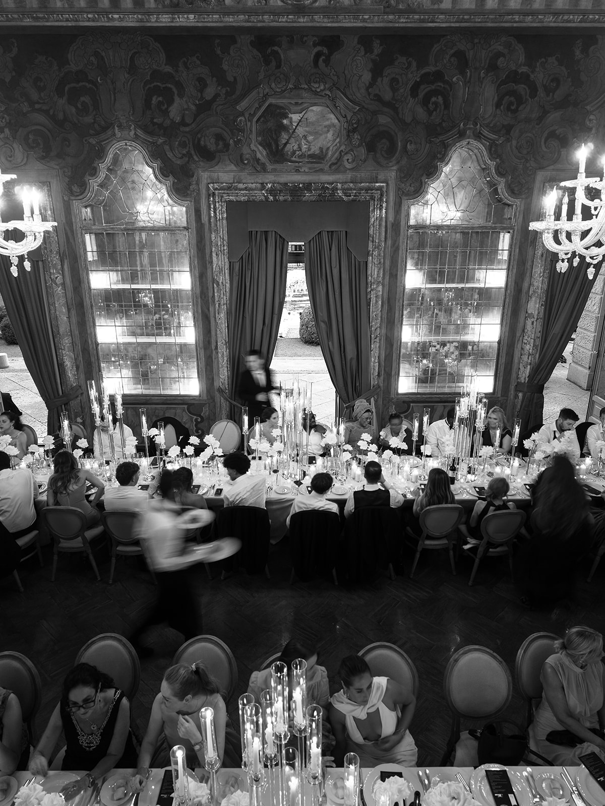 Black and white overhead view of wedding guests dining in Villa Erba's frescoed reception room.
