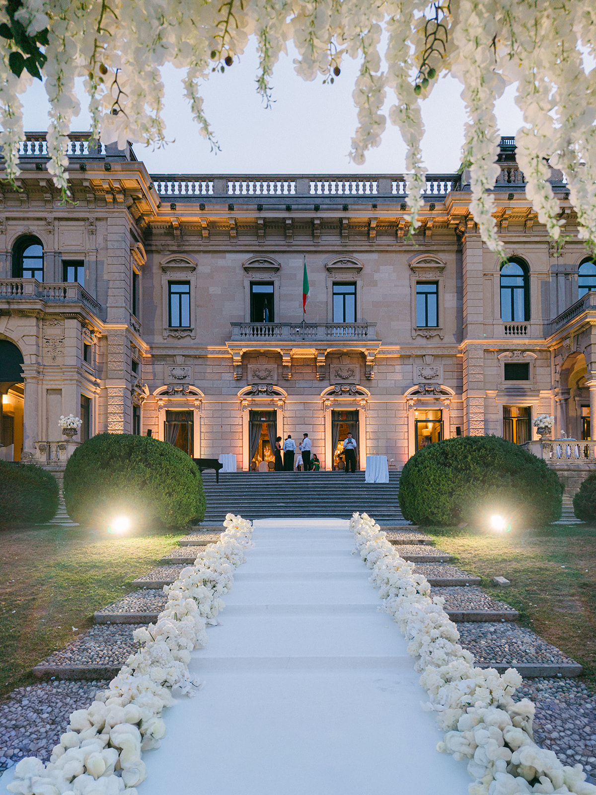 Villa Erba illuminated at dusk, seen from the white floral wedding aisle.